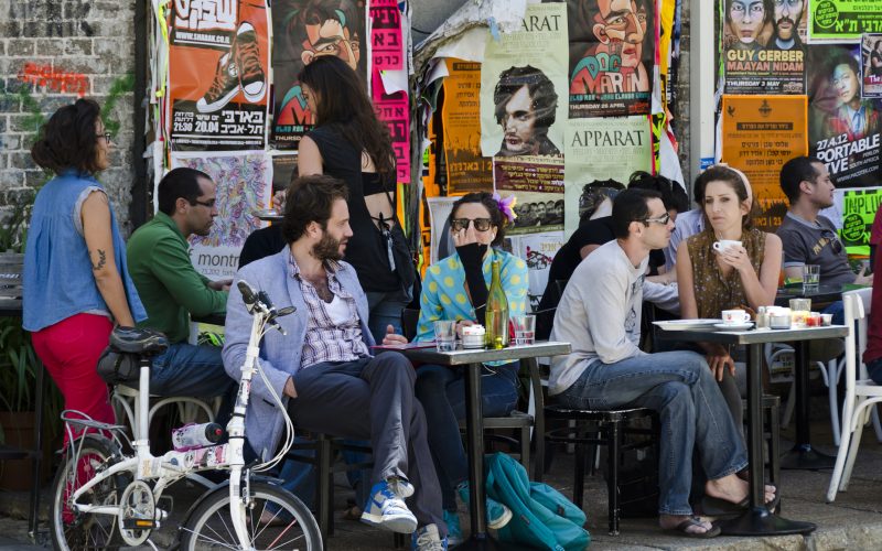 Tel Aviv, Israel - April 20, 2012: People sit and enjoy refreshments and lunch at an outdoor cafe in Tel Aviv on a Friday afternoon. Posters on the wall describe current activities and events taking place in the city.