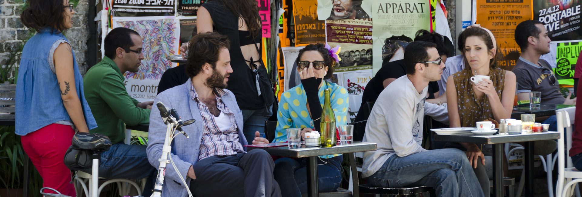Tel Aviv, Israel - April 20, 2012: People sit and enjoy refreshments and lunch at an outdoor cafe in Tel Aviv on a Friday afternoon. Posters on the wall describe current activities and events taking place in the city.