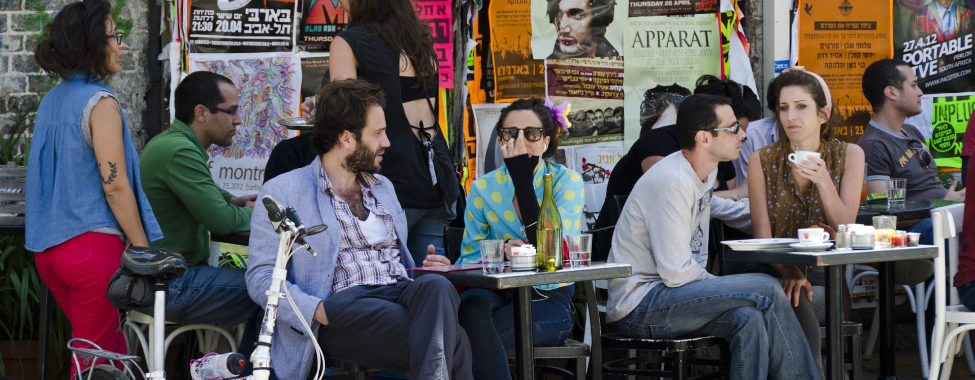 Tel Aviv, Israel - April 20, 2012: People sit and enjoy refreshments and lunch at an outdoor cafe in Tel Aviv on a Friday afternoon. Posters on the wall describe current activities and events taking place in the city.